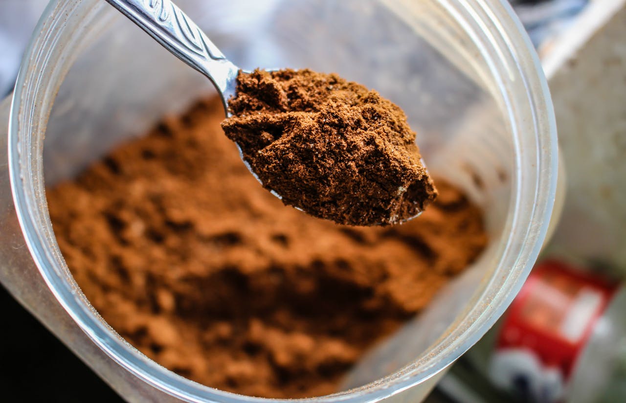 Home Focused shot of a spoon scooping cocoa powder from a container, emphasizing texture.